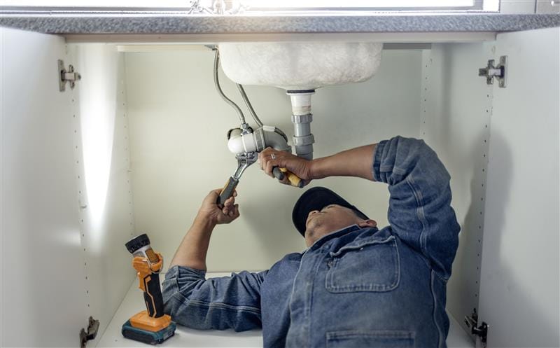 Plumber repairing pipes beneath a bathroom sink in Torrance